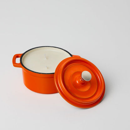 Orange ceramic pot candle with a white interior on a light gray background
