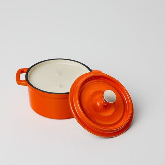 Orange ceramic pot candle with a white interior on a light gray background